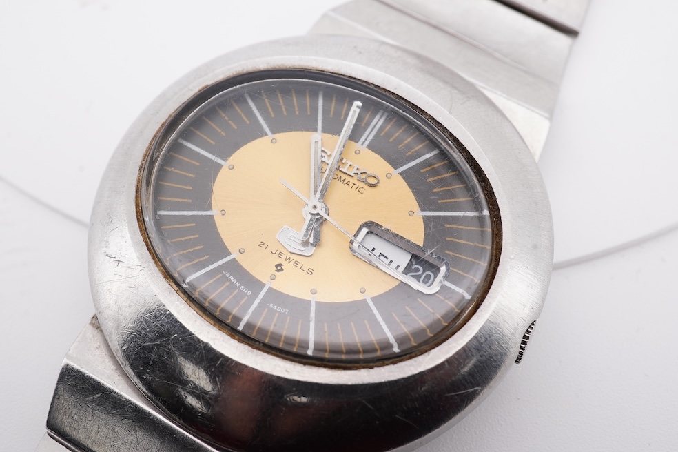 A gentleman's steel Seiko 5 Automatic wrist watch, with oval dial, baton numerals and date aperture, case diameter 40mm, case back numbered 228258, on a stainless steel Seiko bracelet(a.f.), no box or papers. Condition -